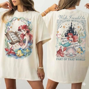 May include: Cream-colored t-shirt featuring a colorful illustration of a mermaid reading sheet music, surrounded by sea creatures. The back of the shirt has a matching design with the text "Wish I could be PART OF THAT WORLD".