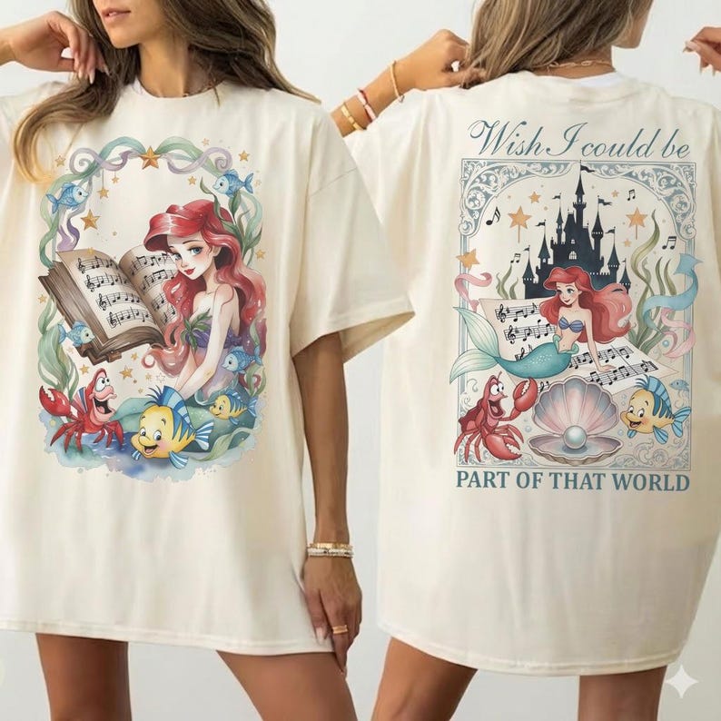 May include: Cream-colored t-shirt featuring a colorful illustration of a mermaid reading sheet music, surrounded by sea creatures. The back of the shirt has a matching design with the text "Wish I could be PART OF THAT WORLD".