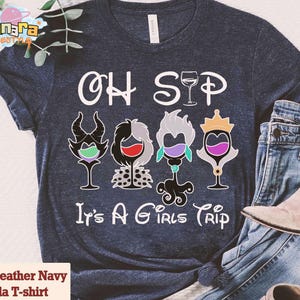 May include: Heather navy Bella T-shirt with the text "OH SIP It's A GIRLS TRIP". The shirt features four wine glass designs with cartoon character elements. The shirt is paired with blue jeans and a beige boot.