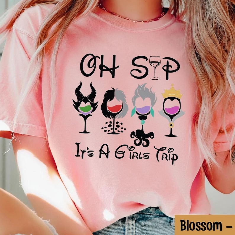 May include: A light pink t-shirt with the words "OH SIP" and "It's A Girls Trip" printed in black. The shirt features four wine glasses with cartoon character designs. The word "Blossom" is printed in a box at the bottom right.