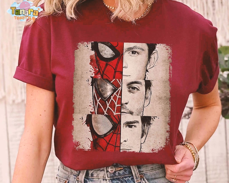 Puede incluir: Camiseta burdeos con un gr&aacute;fico de la m&aacute;scara de Spider-Man y los rostros de tres actores que han interpretado al personaje. El dise&ntilde;o es en rojo, blanco y negro, con un estilo vintage desgastado.