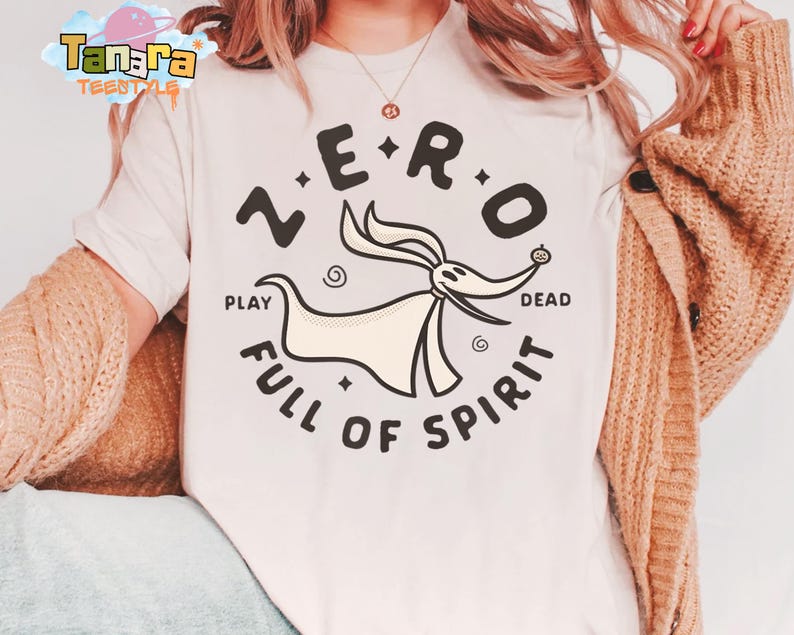 Puede incluir: Camiseta color crema con un gr&aacute;fico circular. El gr&aacute;fico presenta el texto "ZERO" sobre un personaje de dibujos animados parecido a un perro y las palabras "PLAY DEAD FULL OF SPIRIT" debajo. La camiseta es parte de la colecci&oacute;n Tanara TEENSTYLE.