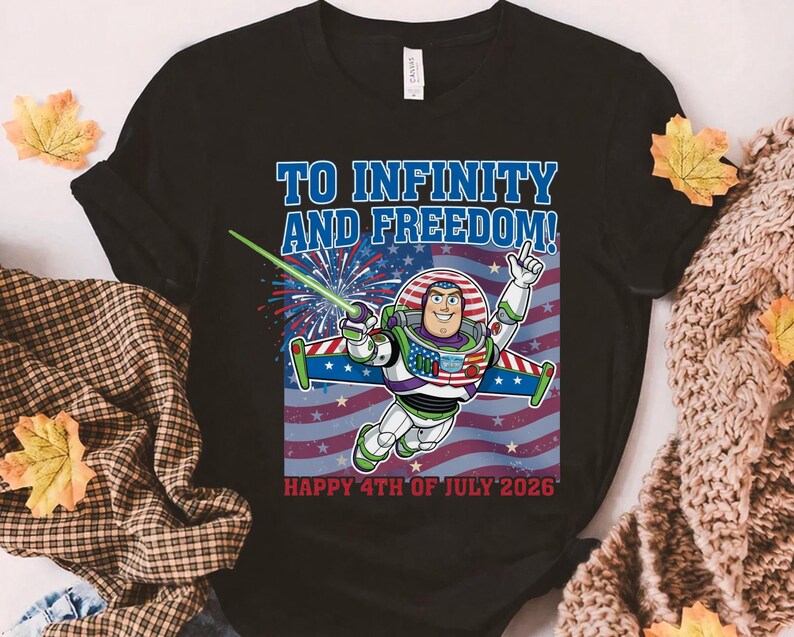 May include: Black t-shirt featuring a graphic of Buzz Lightyear in a patriotic design with the text "TO INFINITY AND FREEDOM!" and "HAPPY 4TH OF JULY 2026". The design includes the American flag and fireworks.