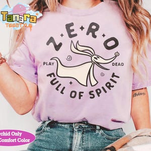 Puede incluir: Una camiseta de color lila claro con un dise&ntilde;o de Zero de Pesadilla antes de Navidad. El dise&ntilde;o incluye las palabras "ZERO", "PLAY", "DEAD" y "FULL OF SPIRIT". La camiseta es de color confort.