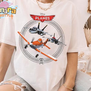 May include: White t-shirt featuring the Disney Planes logo and cartoon aircraft. The design includes the word "PLANES" in red, with three animated planes inside a gray circular design. The shirt has the "Tanara Teenstyle" logo in the upper left corner.