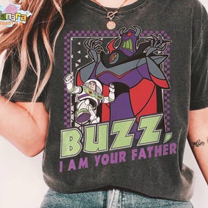 May include: Dark grey t-shirt with a graphic of Buzz Lightyear and Zurg from Toy Story. The design includes the text "BUZZ, I AM YOUR FATHER" in green and purple. The shirt has a vintage, worn appearance.