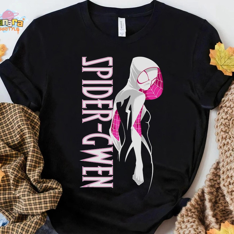 May include: Black t-shirt featuring a stylized illustration of Spider-Gwen in white and pink. The words "SPIDER-GWEN" are printed vertically in pink. The design is a graphic representation of the character's costume.