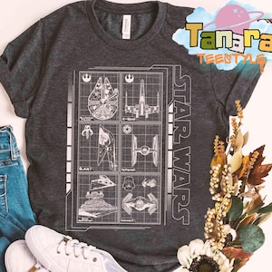 May include: Dark gray Star Wars t-shirt featuring a blueprint design of various spacecraft, including the Millennium Falcon, X-Wing, and TIE Fighter. The words "STAR WARS" are printed vertically on the right side of the shirt. The shirt has a crew neck and short sleeves.