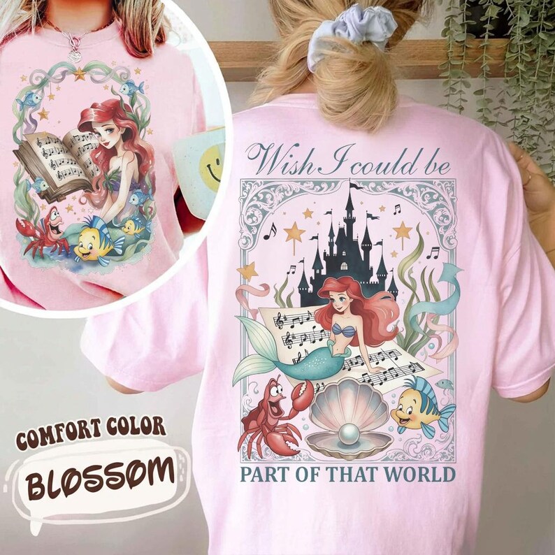 May include: Pink Comfort Color t-shirt featuring a graphic of Ariel from The Little Mermaid. The front shows Ariel with a book and sea creatures. The back has Ariel, a castle, and the text "Wish I could be Part of That World."