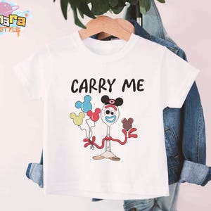 K&ouml;nnte beinhalten: Wei&szlig;es T-Shirt mit dem Text "CARRY ME" in Schwarz. Das Shirt zeigt eine Zeichentrickfigur, die Luftballons h&auml;lt. Die Figur ist ein L&ouml;ffel mit Mickey Mouse-Ohren und roten Armen und Beinen. Die Ballons sind blau, gelb und rot.