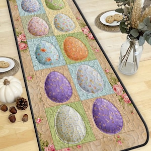 Puede incluir: Alfombra de pasillo con diseño de patchwork. Presenta coloridos huevos de Pascua en varios patrones, sobre un fondo beige y verde con detalles florales. La alfombra es rectangular con un borde negro. La longitud es de aproximadamente 150 cm.