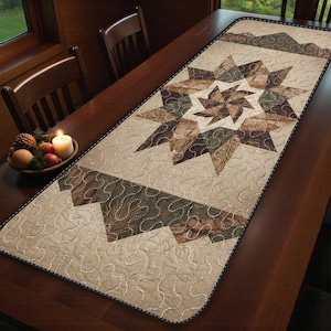 May include: A beige quilted table runner with a central starburst design in shades of brown and green. The runner features a geometric pattern and decorative stitching, adding a rustic touch to the table setting.
