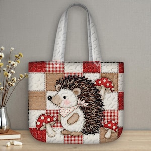 Peut inclure: Sac fourre-tout matelassé avec une illustration de hérisson et des champignons à pois rouges et blancs. Le sac a un motif patchwork avec du vichy rouge et des carrés blancs, et une poignée blanche.