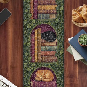 May include: A decorative runner featuring a stacked book design with arched openings. Each arch showcases a stack of books and a sleeping cat. The design is framed by green ivy and a stitched border, creating a cozy, literary theme.