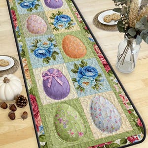 May include: Easter-themed table runner featuring a patchwork design with floral and egg motifs. The runner showcases pastel-colored eggs with bows and floral arrangements in shades of blue, pink, and orange. The edges are adorned with a floral border.