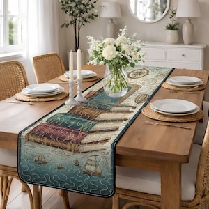 May include: A rectangular table runner with a nautical and literary theme. The runner features a design of stacked antique books, ships, and a map. The colour palette includes shades of blue, brown, and cream. The runner is placed on a wooden dining table.