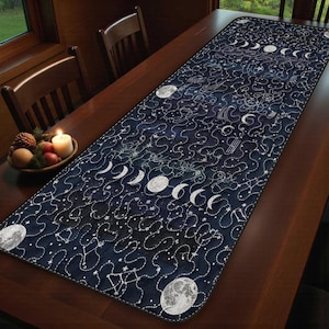 Puede incluir: Camino de mesa azul oscuro con un diseño celestial que presenta fases lunares, constelaciones y estrellas. El camino de mesa rectangular tiene un aspecto acolchado con costuras blancas. El diseño está impreso en la tela.