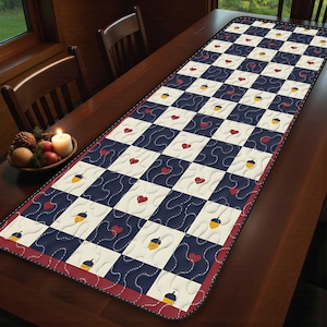 以下が含まれることがあります： ネイビーブルーとクリーム色の市松模様のキルトテーブルランナー。正方形には赤いハートと黄色のドングリが飾られています。ランナーは赤い縁取りがあり、木製のテーブルの上に置かれています。