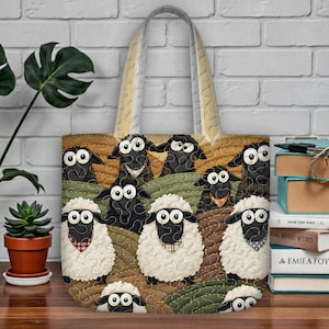 Puede incluir: Bolso tote acolchado con un diseño caprichoso de ovejas en colinas onduladas. El bolso tiene un asa beige y un patrón repetido de ovejas blancas y negras con ojos grandes. El fondo es un mosaico de verde, marrón y beige.
