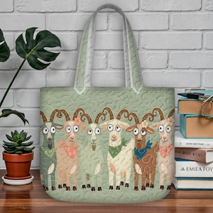 May include: A light green tote bag with a quilted pattern and a row of cartoon goats. Each goat has a unique color and bandana. The bag has a light green handle and is sitting on a wooden surface.