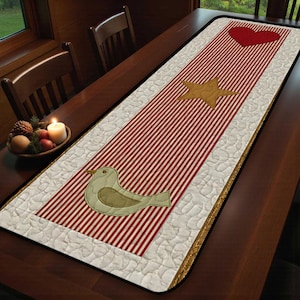 May include: A rectangular table runner with a red and white striped center. The runner features appliqued shapes including a red heart, a gold star, and a bird. The border is a quilted white fabric with a gold trim. The runner is placed on a wooden table.