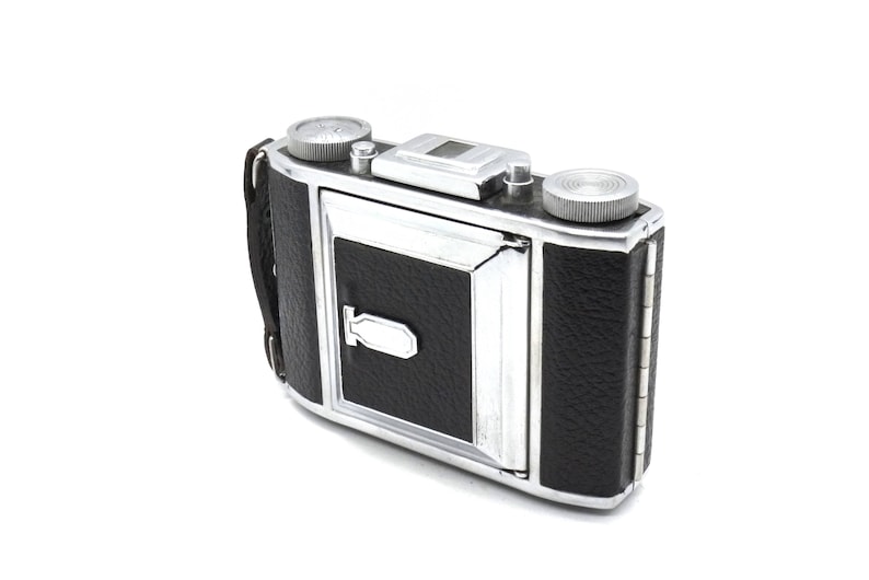 May include: A vintage silver and black 35mm film camera with a leather covering. The camera has a built-in flash and a viewfinder.