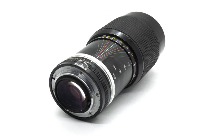 Puede incluir: Un objetivo de c&aacute;mara negro con un anillo plateado y una escala en blanco y negro. La escala muestra la distancia focal en mil&iacute;metros, de 85 a 200.