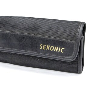 May include: Black canvas carrying case with a leather flap and the word "SEKONIC" printed in gold lettering.