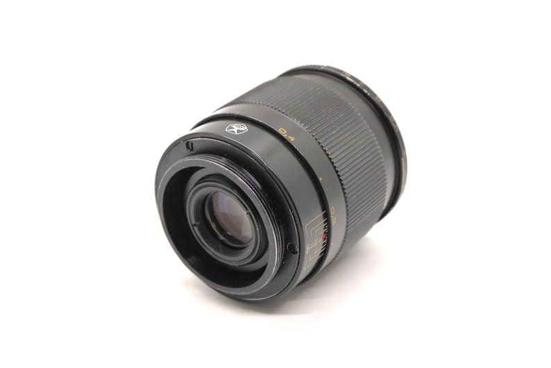 K&ouml;nnte beinhalten: Ein schwarzes Kameraobjektiv mit einem silbernen Ring und Markierungen. Das Objektiv hat einen schwarzen Gummiring um die Vorderseite.