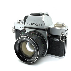 May include: A silver and black Ricoh TLS 400 SLR camera with a black 21/50.3 Ricoh Xenon lens attached. The camera has a black leatherette covering on the body.