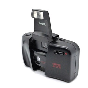 May include: A black Kodak Star 435 film camera with a built-in flash. The flash is raised and the camera lens is visible.