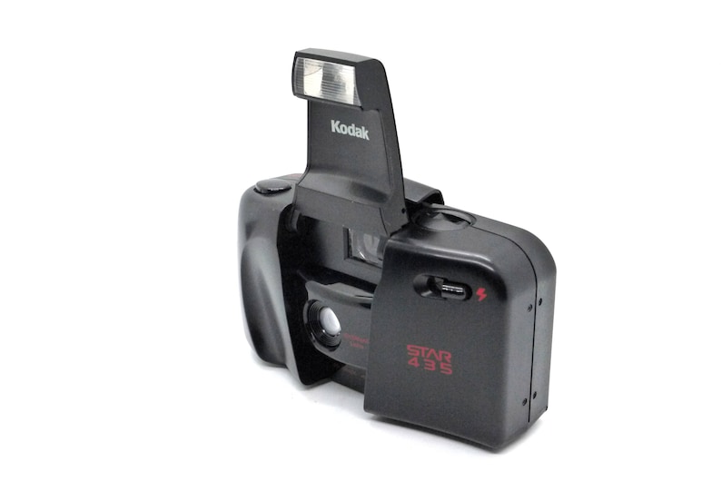 May include: A black Kodak Star 435 film camera with a built-in flash. The flash is raised and the camera lens is visible.