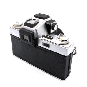 May include: A silver and black 35mm film camera with a black leather covering. The camera has a built-in light meter and a manual focus lens.