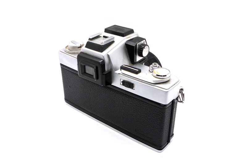 May include: A silver and black 35mm film camera with a black leather covering. The camera has a built-in light meter and a manual focus lens.