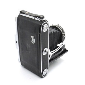 Puede incluir: Una c&aacute;mara plegable negra y plateada con fuelle y cubierta de cuero. La c&aacute;mara tiene un acabado cromado y una correa de cuero.