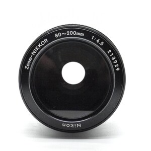 Puede incluir: Un objetivo Nikon Zoom-Nikkor negro con el texto "80~200mm 1:4.5 213929" impreso en el lateral.