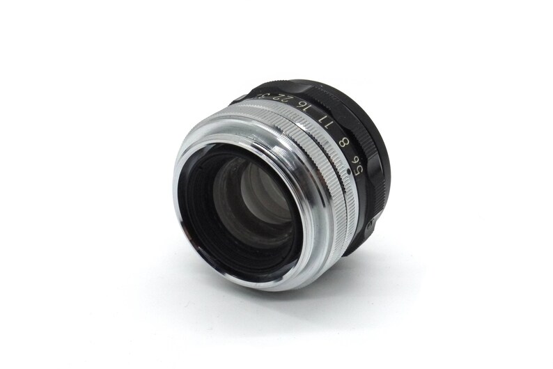 May include: A silver and black camera lens with an aperture ring that reads "5.6 8 9 11 16 22 27 32".