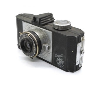 Puede incluir: C&aacute;mara UniveX vintage en blanco y negro. La c&aacute;mara tiene una lente, un dial plateado y un cuerpo plateado y negro. Las palabras "UniveX" e "IRIS" est&aacute;n impresas en el lateral. La c&aacute;mara est&aacute; sobre un fondo blanco.