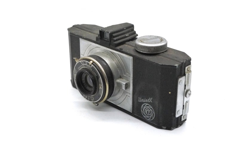 Puede incluir: C&aacute;mara UniveX vintage en blanco y negro. La c&aacute;mara tiene una lente, un dial plateado y un cuerpo plateado y negro. Las palabras "UniveX" e "IRIS" est&aacute;n impresas en el lateral. La c&aacute;mara est&aacute; sobre un fondo blanco.