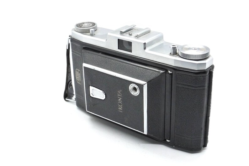 Puede incluir: Una c&aacute;mara Ikonta plateada y negra con una cubierta de cuero. La c&aacute;mara tiene una lente plateada y una correa de cuero negra.