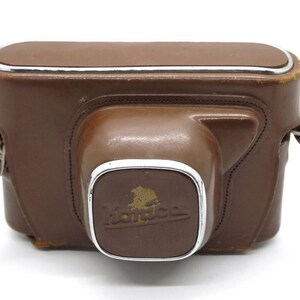 Op de afbeelding: Een bruine leren cameratas met een zilveren metalen rand en een band. De tas heeft het woord "Kodak" in reli&euml;f op de voorkant.