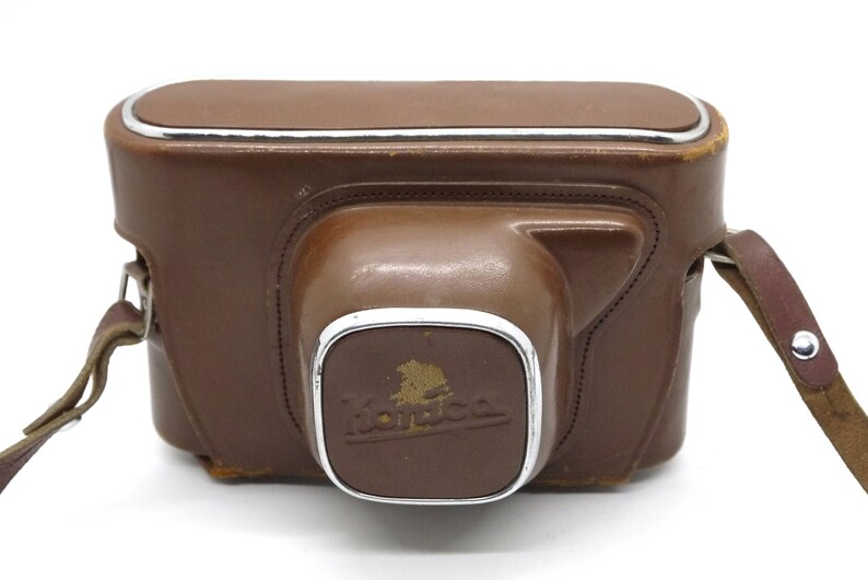 Op de afbeelding: Een bruine leren cameratas met een zilveren metalen rand en een band. De tas heeft het woord "Kodak" in reli&euml;f op de voorkant.