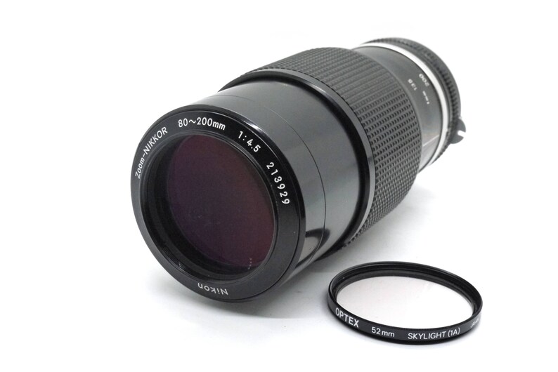 Puede incluir: Un objetivo Nikon Zoom-Nikkor 80-200mm 1:4.5 negro con un filtro Optex Skylight (1A) de 52 mm negro.