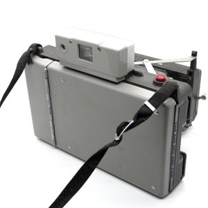 May include: A gray Polaroid camera with a black strap. The camera has a red button on the side and a white flash unit on top.
