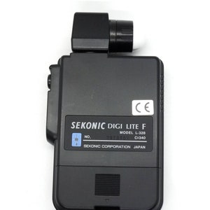 May include: Black Sekonic Digi Lite F light meter with a CE mark, model number L-328, and serial number 0070107. The light meter is made by Sekonic Corporation in Japan.