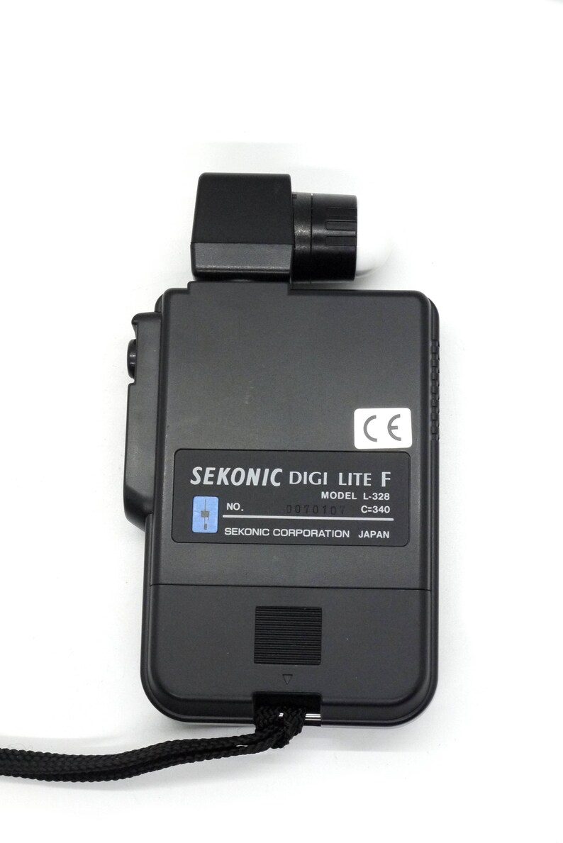 May include: Black Sekonic Digi Lite F light meter with a CE mark, model number L-328, and serial number 0070107. The light meter is made by Sekonic Corporation in Japan.