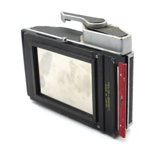 Puede incluir: Una c&aacute;mara negra y plateada con un porta-carretes rojo. La c&aacute;mara tiene un visor y una palanca en la parte superior. El porta-carretes tiene el texto "P60/25 - 2242015 MADE IN JAPAN" impreso en &eacute;l.