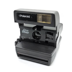 Peut inclure: Un appareil photo instantané Polaroid OneStep noir avec un flash intégré. L'appareil photo possède un viseur et un cache d'objectif.