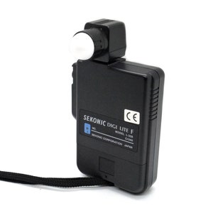 May include: A black Sekonic Digi Lite F light meter with a white dome on the top. The meter has a black strap and the text "SEKONIC DIGI LITE F MODEL L-328 C340 SEKONIC CORPORATION JAPAN" is printed on the side.