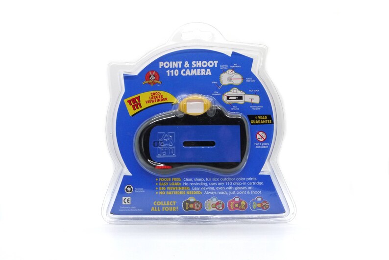 May include: A blue and black point and shoot 110 camera with a yellow viewfinder. The packaging says "Try Me!" and "100% Larger Viewfinder".